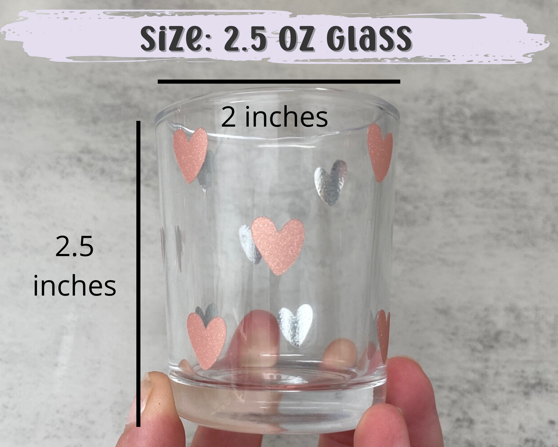 daisy shot glass in someones hand to show the size, 2.5oz and 2.5inches in height and 2 inches in width, has a heart design on it in rose gold