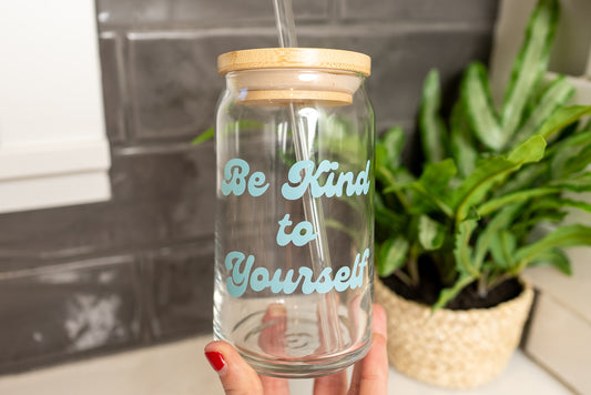 be kind to yourself glass cup with bamboo lid and clear glass straw, minimalist background with green plant, self care tumbler, positive mindset design