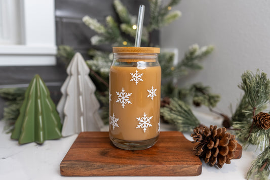 iced coffee glass cup with white snowflakes on it, pictured with a bamboo lid and clear glass straw with a christmas decor background