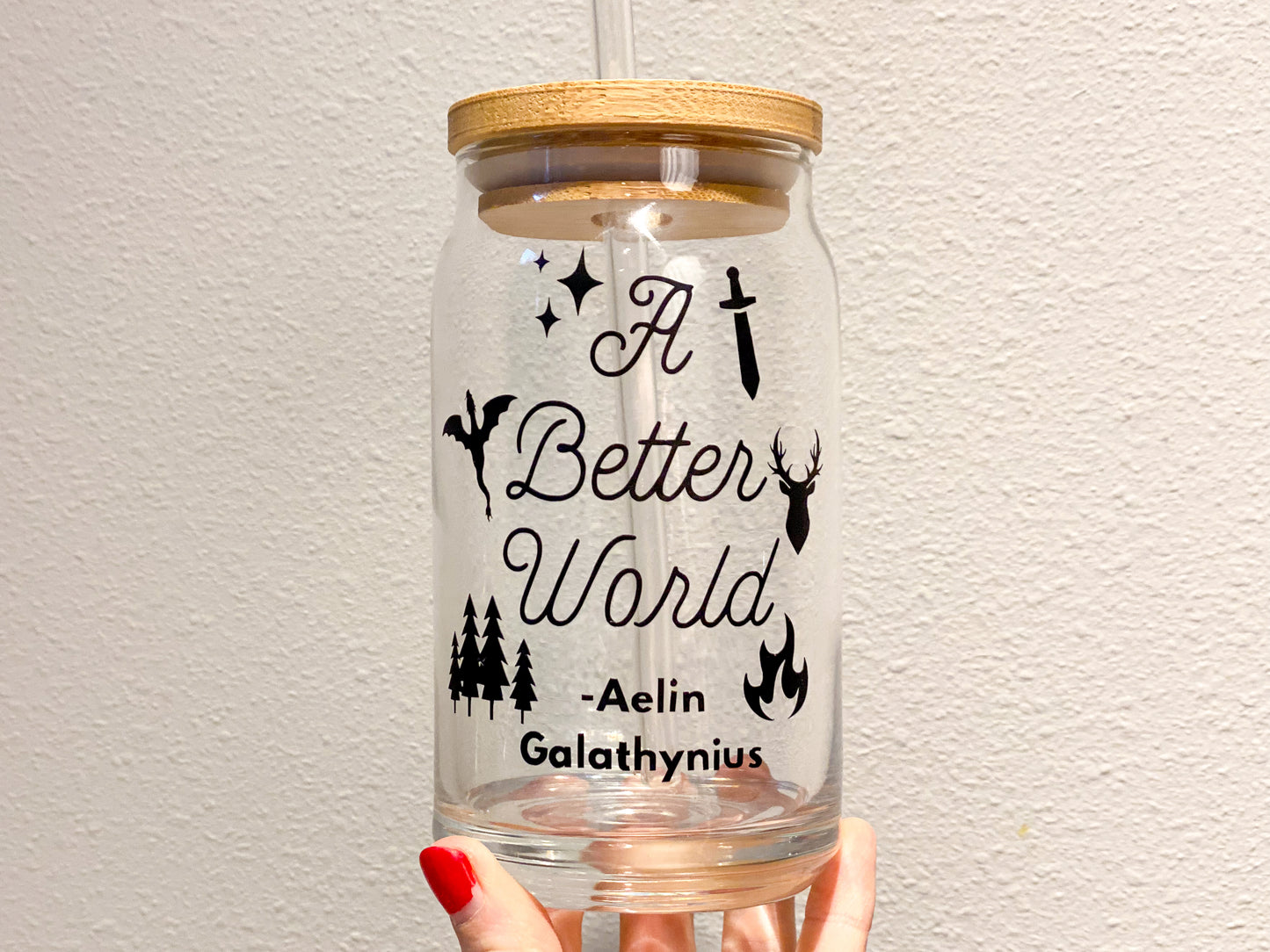 Glass cup for throne of glass book lovers with the quote from aelin galathynius that says a bettwe rold with 6 icons of stars, sword, wyrven, stag, pine trees, and fire on it, all in a black font, white  background with cup in hand