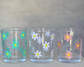 3 shot glasses with a daisy flower design on it in mint, rose gold, and white with yellow dots in the middle, minimalist background